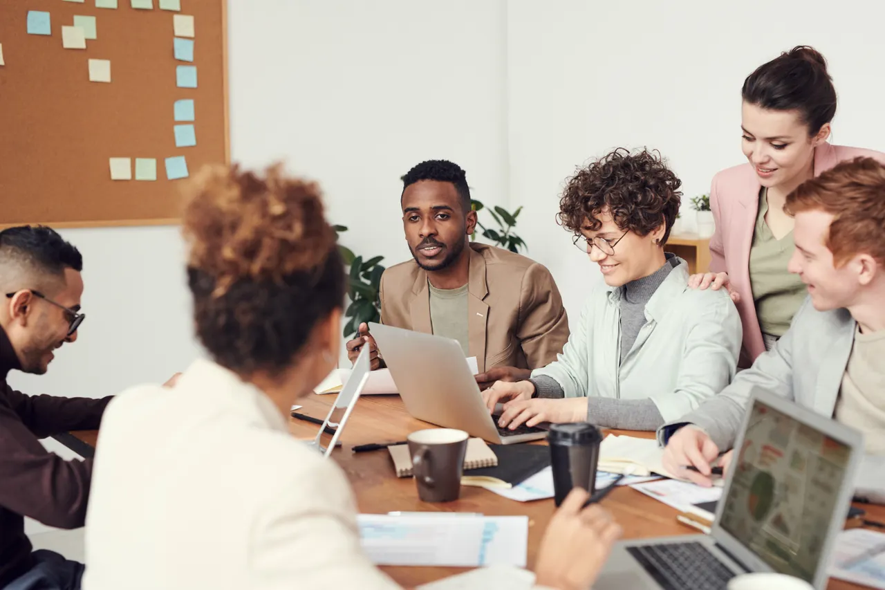 A marketing team in discussion around a meeting table with laptops in a bright, modern office